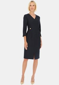 Granatowa sukienka z dekoltem w serek, rękawami do trzech czwarte i rozporkiem z przodu. Posiada dwie boczne kieszenie z ozdobnymi złotymi guzikami.