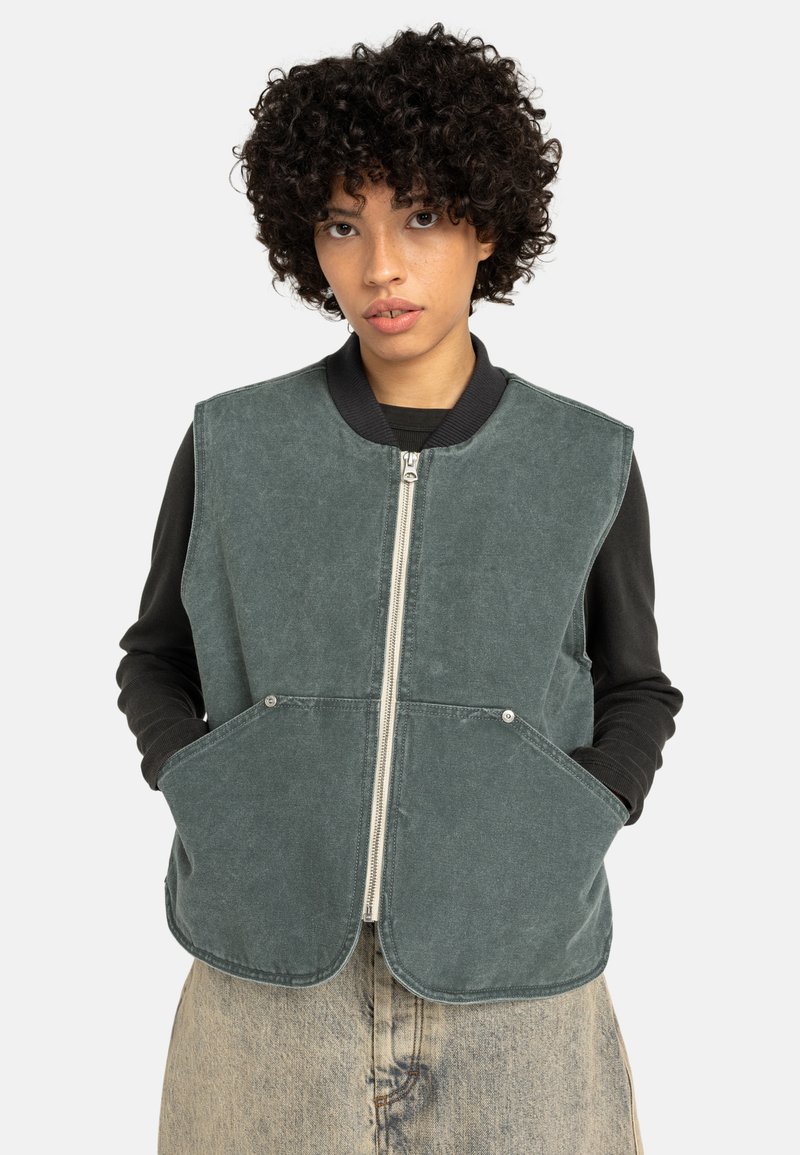 Groen, dik katoenen vest met een afgeronde zoom, zilveren ritssluiting, twee zijzakken en een geribde halslijn. Draagt over een zwart shirt met lange mouwen.