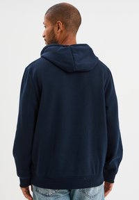 Sudadera azul marino hecha de suave algodón, con una gran capucha, mangas largas y un dobladillo acanalado. Sin patrones ni acentos visibles.