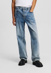 Lichtblauwe denim jeans met een relaxte pasvorm, vervaagde textuur, vijf zakken ontwerp en rechte pijpen, gecombineerd met zwarte schoenen.