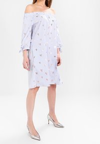 Olkapäältä tippuva mekko, jossa on sinivalkoiset raidat, koristeltu metallinhohtoisilla sydänkuvioilla, ja jossa on kolme neljäosaa hihat sekä nauhat hihoissa.