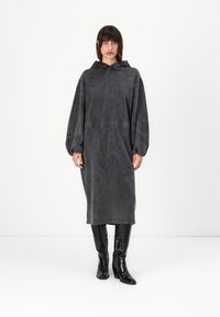 Oversized gray hooded dress made of denim-like fabric, featuring a cinched waist and long sleeves with elastic cuffs. Black tall boots.