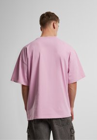 Ružićasta oversized majica, kratki rukavi, okrugli izrez. Mekani pamučni materijal s glatkom teksturom, prikazana sa stražnje strane.