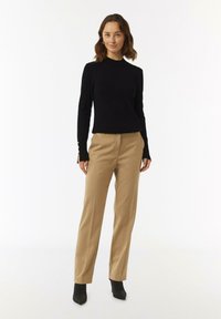 Zwarte gebreide trui met een hoge hals, gecombineerd met beige op maat gemaakte broeken. De outfit wordt compleet gemaakt met zwarte enkellaarzen.