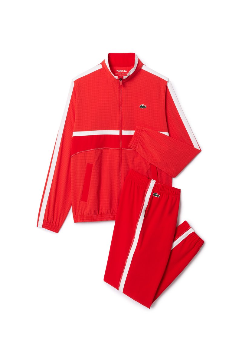 Survêtement rouge composé d'une veste zippée avec des rayures blanches et un pantalon assorti, featuring un tissu texturé et des accents du logo Lacoste.