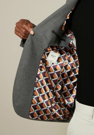 Grauer Blazer aus strukturiertem Außenmaterial, mit einem hell gemusterten Satinfutter in geometrischen Formen von Lila, Orange und Blau.