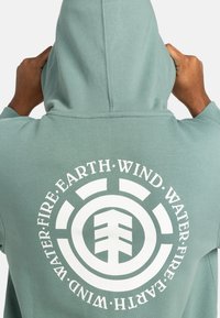 Light green hoodie with a centered white circular graphic and text. Front has a hood; material appears soft with a smooth texture.