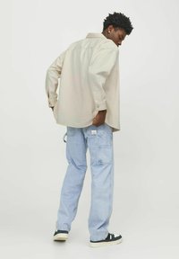 Beige button-up shirt, relaxed fit, with cuffed sleeves; light blue cargo jeans with pockets; black and white sneakers.