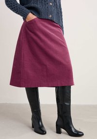 Bordeaux knielange rok met zijzakken, gemaakt van een textuurstof, gecombineerd met zwarte kniehoge laarzen met hak, met een gladde afwerking.
