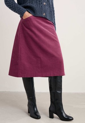 Jupe longueur genou bourgogne avec poches latérales, en tissu texturé, associée à des bottes noires à talons hauts arrivant au genou, avec une finition lisse.