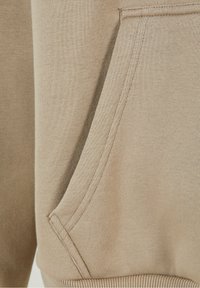 Sudadera color marrón con bolsillo visible y costuras a la vista, de tejido texturizado. Presenta una costura lateral y un puño acanalado en la parte inferior.