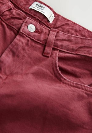 Baggy low-rise pants in a deep burgundy color, made from cotton fabric. Features a front pocket, button closure, and stitching details.