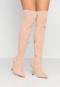 Blushrosa över knäboots i mjuk mocka med spetsig tå och metallisk stilettklack. Har en sidogylf för enkel på- och avtagning.