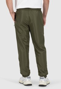 Olijfgroene, lichte, elastische taillebandbroeken met taps toelopende pijpen en enkelmanchetten, gedragen met witte en grijze sneakers.