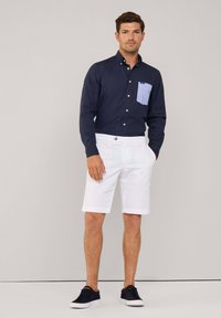 Navyblauwe overhemd met knopen en een lichtblauwe zak, gecombineerd met witte shorts en donkere sneakers. Gladde stof en slim fit.