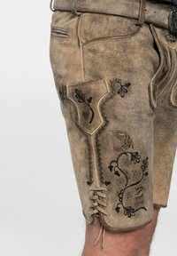 Bruine leren shorts zijn voorzien van ingewikkelde zwarte bloemenborduursels en een traditioneel ontwerp. Ze hebben een zijzak met decoratieve stiksels.