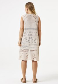 Ärmelloses Strickkleid in Beige mit Openwork-Mustern, unterschiedlichen Texturen und geometrischen Designs. Knielang, seitliche Schlitze für Bewegungsfreiheit.