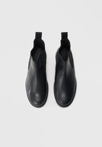 Černé kožené kotníkové boty Chelsea s elastickými bočními panely, zaoblenými špičkami a poutky na snadné nazouvání; hladká textura a prošití kolem podrážky.