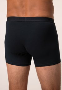 Boxer in cotone nero con vita elasticizzata, design fitted, texture liscia e dettagli di cucitura minimi. Vista posteriore mostrata.