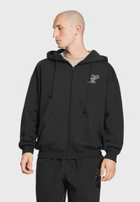 Czarny hoodie na zamek, wykonany z miękkiego materiału, z przednią kieszenią, sznurkami w kapturze oraz logo na klatce piersiowej. Prosty design.