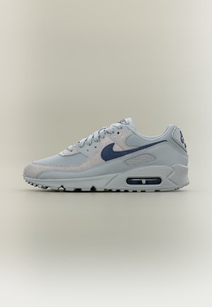Baskets Nike Air Max gris clair avec logo swoosh bleu foncé et coussinet d’air visible dans la semelle sur un fond neutre et simple.