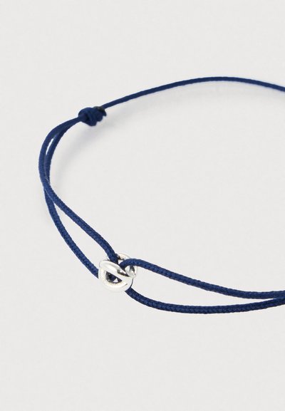 Gaiši zilā krāsā regulējama aukliņa aproce ar mazu sudraba cilpas mezglu sprādi uz vienkārša balta fona.