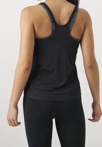 Débardeur de sport noir avec bretelles réglables et texture lisse, associé à un legging noir, mettant en valeur une coupe ajustée.