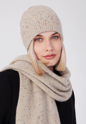 Ensemble bonnet et écharpe en beige avec des éclats multicolores. Texture douce, motif côtelé sur le bonnet, écharpe drapée avec de légers plis.