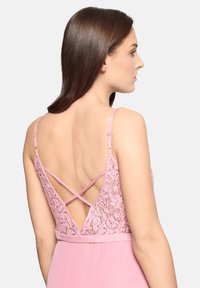 Robe rose avec un dos en dentelle à bretelles croisées, jupe fluide et corsage ajusté. Le tissu est léger avec une texture douce.