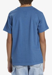 Modré tričko s krátkým rukávem vyrobené z bavlny, s kulatým výstřihem a tištěným logem na zadní straně; hladká textura a běžný střih.