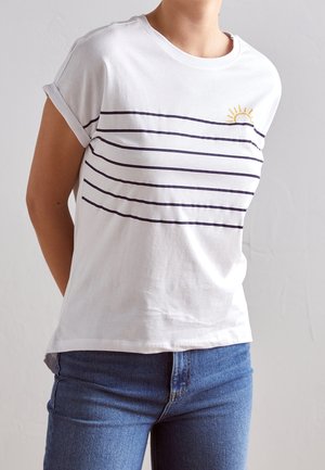 Biały bawełniany t-shirt z granatowymi poziomymi paskami i małym żółtym wzorem słońca blisko lewego ramienia. Krótkie podwinięte rękawy i luźny krój.