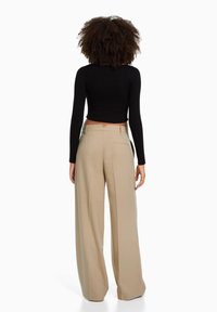 Czarny prążkowany top z długim rękawem w połączeniu z beżowymi spodniami o szerokich nogawkach z wysokim stanem, które mają tylną kieszeń i szczegół w postaci wycięcia na pasku.