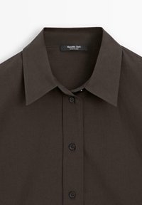 Chemise marron foncé boutonnée avec un col pointu classique et une étiquette de marque visible à l'intérieur de l'encolure.