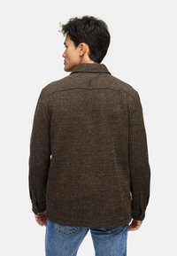 Brun ribbad jacka med krage, långa ärmar och knäppningar vid manschetterna. Bärs med blå jeans, vilket visar en strukturerad textil.
