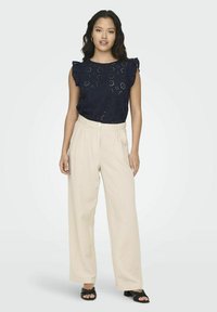 Top ricamato blu navy con maniche a volant, abbinato a pantaloni beige a gamba larga e scarpe nere senza lacci. Design semplice e texture morbida.