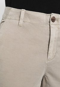Pantaloni in cotone beige con fronte piatto, due tasche laterali e un singolo bottone in vita, caratterizzati da dettagli di cucitura discreti.
