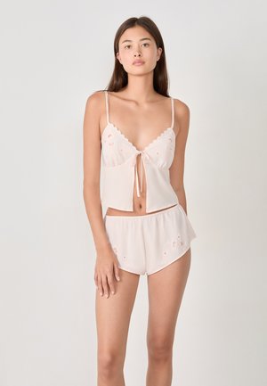 Completo di lingerie in satin rosa chiaro con bordi scallopati, motivi floreali ricamati e top annodato, abbinato a pantaloni corti coordinati.
