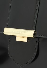 Borsa a mano in pelle verniciata nera con una chiusura rettangolare dorata e cuciture dettagliate. Texture liscia con un design a pattina appuntita.