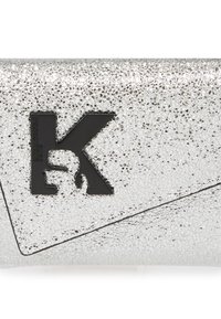 Strieborná klopňová taška s trblietavým povrchom, s čiernym embosovaným logom "K" a uhlovým dizajnom klapky. Kompaktný a štíhly vzhľad.