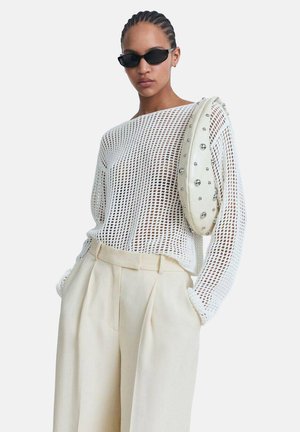 White mesh sweater with long sleeves, paired with cream pleated trousers and a white handbag featuring silver studs. Black sunglasses complete the look.