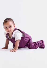 Lila wasserdichte Latzhose aus glattem, flexiblem Material mit verstellbaren Trägern, kombiniert mit einem weißen T-Shirt mit kurzen Ärmeln.