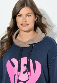 Granatowa bluza z dużym różowym nadrukiem z napisem „HEY.” Ma beżowy kaptur i ściągacze do regulacji.
