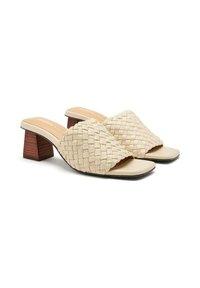 Mules de tacón bloque tejido en beige con una tira ancha, que presentan una plantilla de cuero suave y un tacón de madera texturizado.