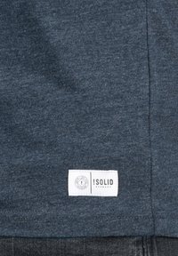 Camiseta de algodón azul oscuro con una textura suave y una etiqueta de marca blanca en la parte inferior que muestra "!SOLID DENMARK" y un logotipo.