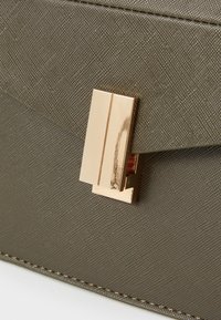 Oliivivihreä kuvioitu clutch-laukku, jossa on kultasävyinen saranaklipsi ja litteä läppäsulku. Sujuva materiaali, jossa on yksityiskohtaisia pistoja.