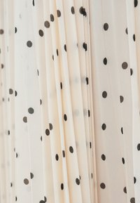 Crèmekleurige geplooide stof met zwarte polka dots. De textuur lijkt licht en doorschijnend, wat zorgt voor een zacht, vloeiend ontwerp.