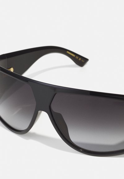 Crne sunčane naočale sa elegantnim okvirom, tamnim gradijentnim staklima i blago zakrivljenim stranicama koje imaju mali zlatni emblem.