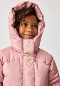 Lyserød polstret jakke med høj hætte, som har guldtekst på forsiden, glat tekstur og et varmt design, der er velegnet til koldt vejr.