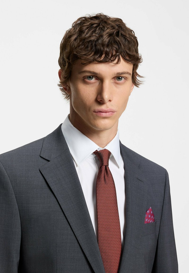 Gray suit with a notched lapel, white shirt, and a textured burgundy tie. A patterned burgundy pocket square accents the breast pocket.