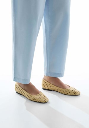 Ballerine perforate gialle con punta arrotondata e suola nera bassa, abbinate a pantaloni blu chiaro.